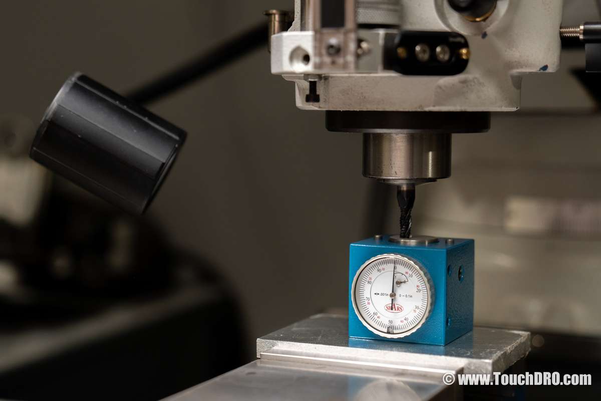 Fig. 1: An inexpensive dial tool height setter in use; the cutter is lowered onto the anvil until the dial reads zero An inexpensive dial tool height setter on the milling machine table, with an end mill lowered onto its anvil