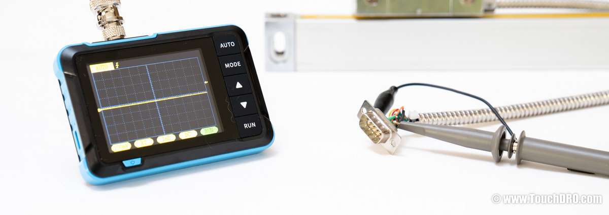 Pinout reverse-engineering setup for an unknown DRO scale: handheld oscilloscope, DB-9 connector with exposed wiring, and a glass linear scale on a workbench