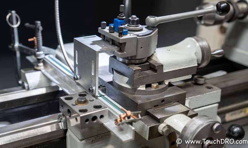 The reference scale clamped across the ways, with the reading head held in the tool post Glass reference scale clamped across the lathe ways with the reading head held in the tool post for magnetic scale calibration
