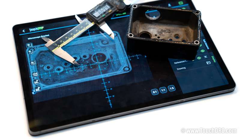 A tablet running TouchDRO with a photo of an enclosure aligned in the graphical view, with the enclosure and a caliper sitting on the tablet